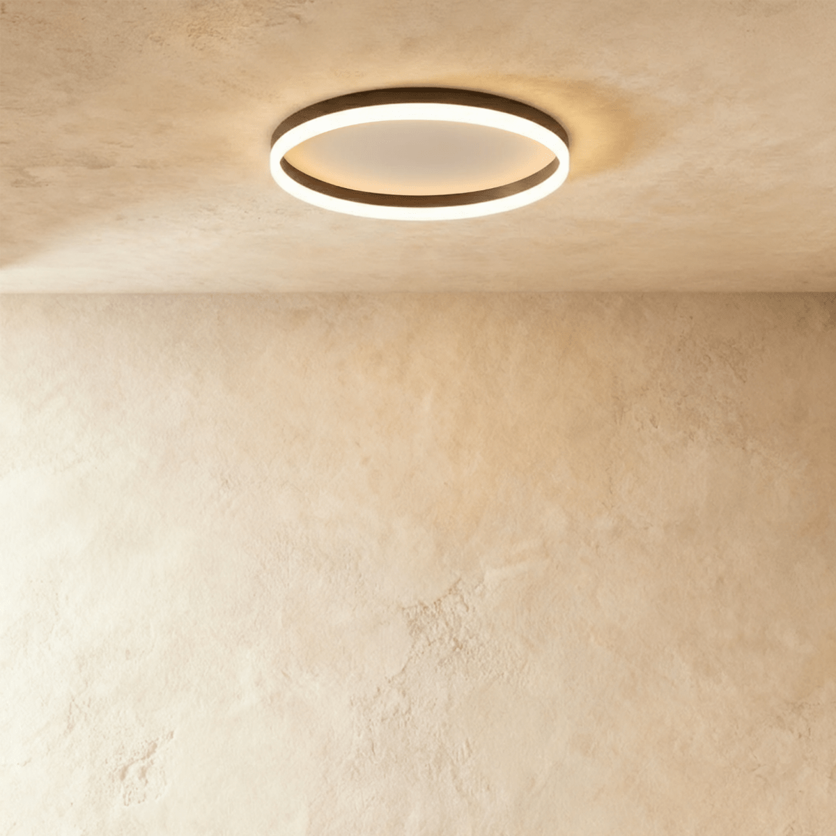 Clérachic slim black round ceiling light with a glowing acrylic ring and pale centre disc, flush on limewash plaster.