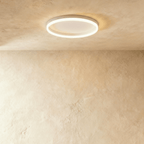 Clérachic slim white round ceiling light with a glowing acrylic ring and pale centre disc, flush on limewash plaster.