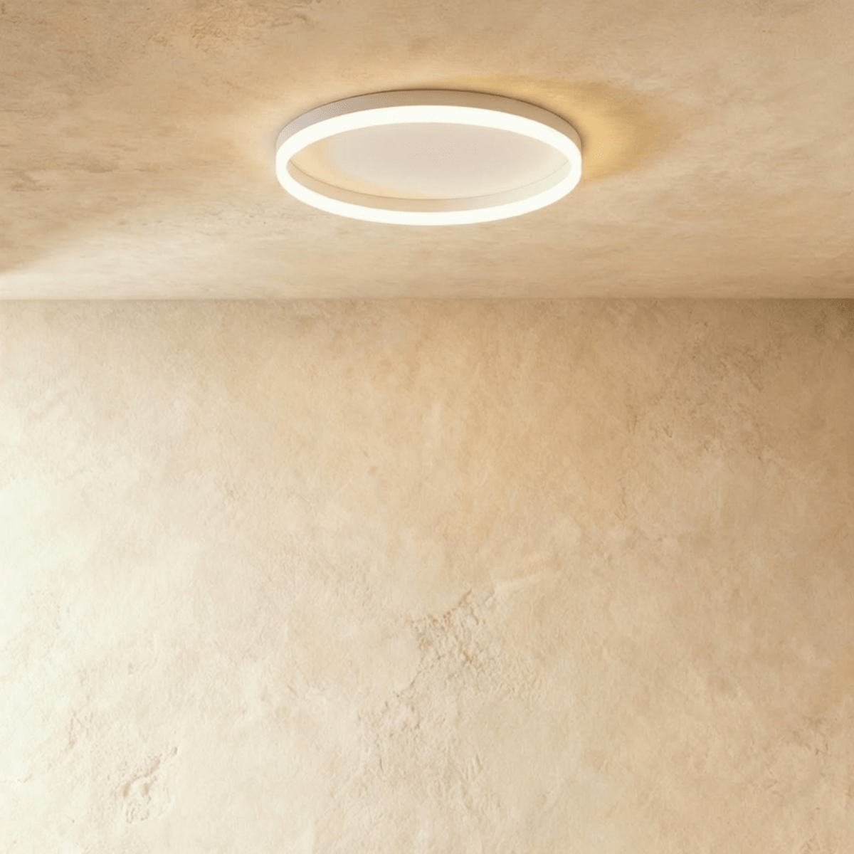 Clérachic slim white round ceiling light with a glowing acrylic ring and pale centre disc, flush on limewash plaster.