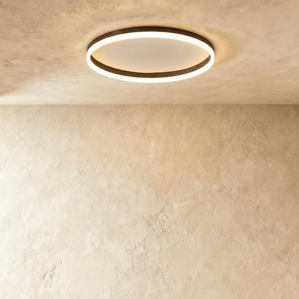 Clérachic slim black round ceiling light with a glowing acrylic ring and pale centre disc, flush on limewash plaster.