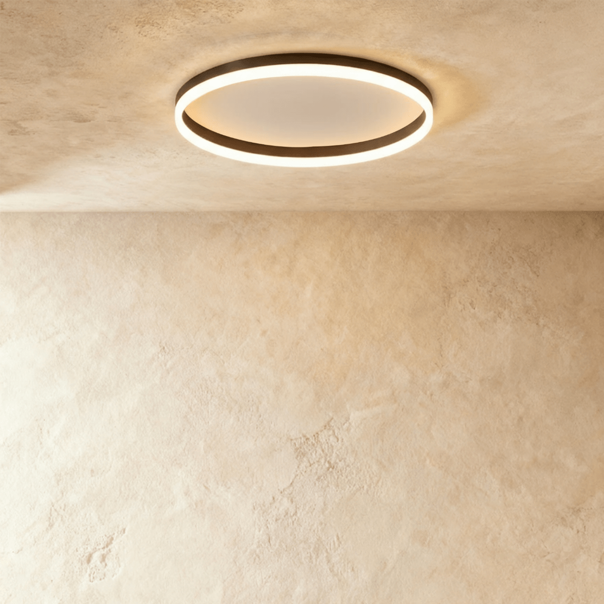 Clérachic slim black round ceiling light with a glowing acrylic ring and pale centre disc, flush on limewash plaster.