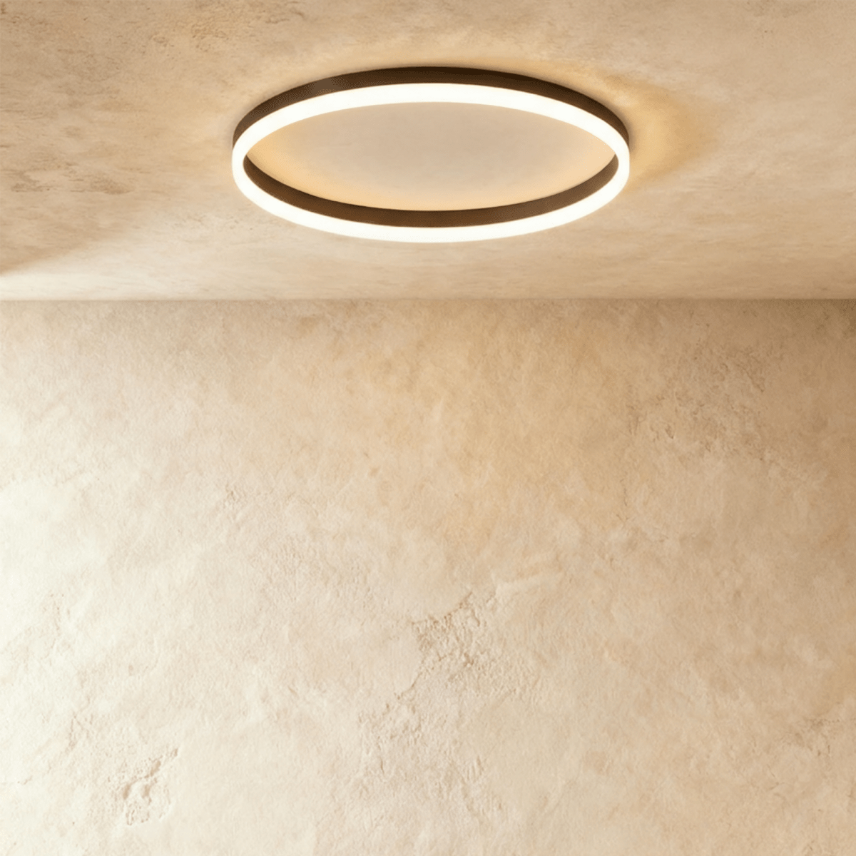 Clérachic slim black round ceiling light with a glowing acrylic ring and pale centre disc, flush on limewash plaster.