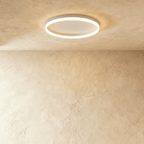 Clérachic slim white round ceiling light with a glowing acrylic ring and pale centre disc, flush on limewash plaster.