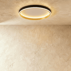 Clérachic black round ceiling light with a glowing acrylic ring and a brushed gold inner wall, flush on limewash plaster.