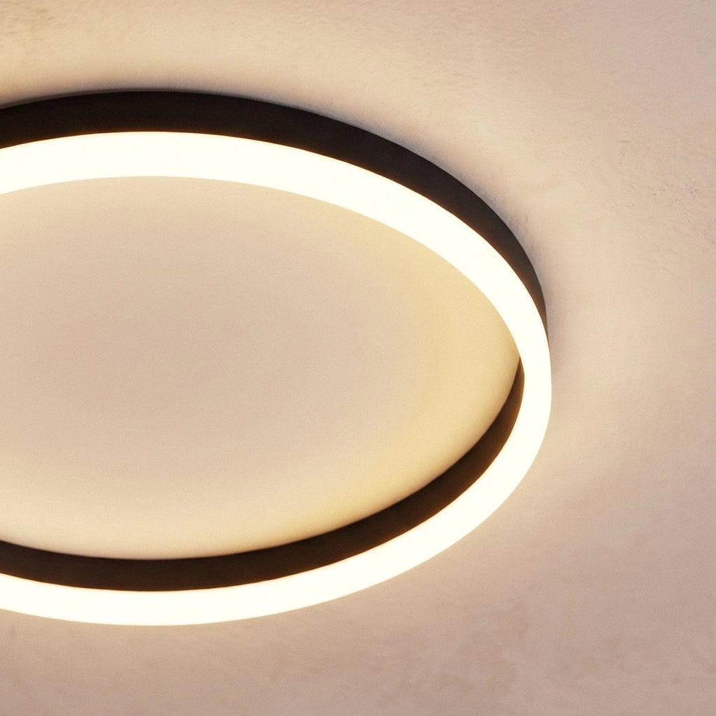 Clérachic close view of a black round ceiling light, its frosted acrylic ring glowing around a pale recessed centre disc.