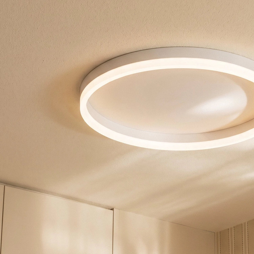 Clérachic close view of a slim white round ceiling light, its glowing acrylic ring and shallow metal rim on a textured ceiling.