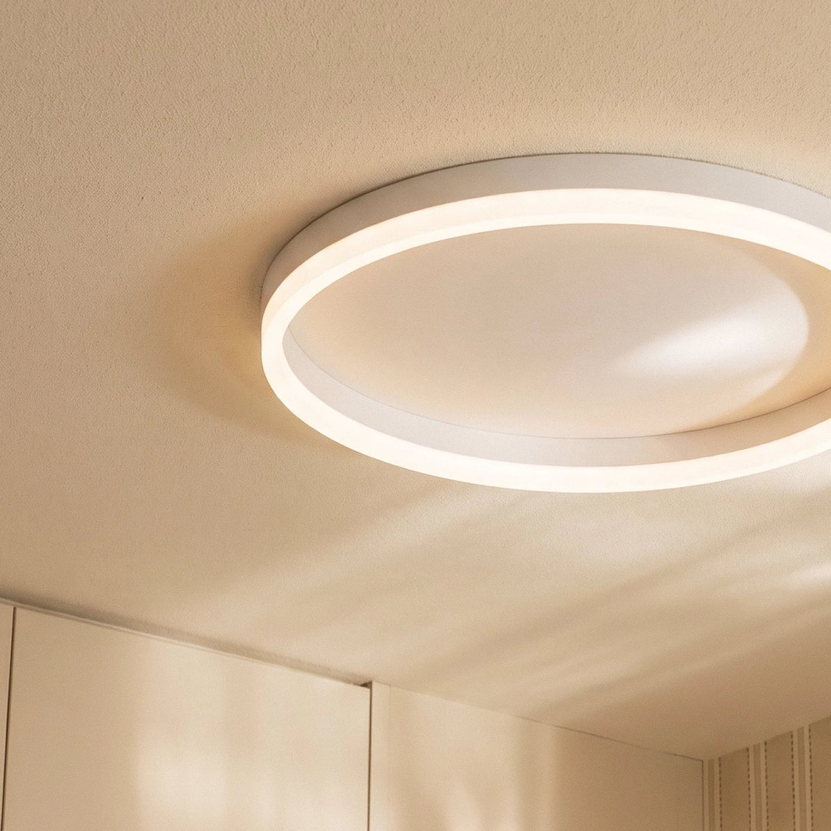Clérachic close view of a slim white round ceiling light, its glowing acrylic ring and shallow metal rim on a textured ceiling.