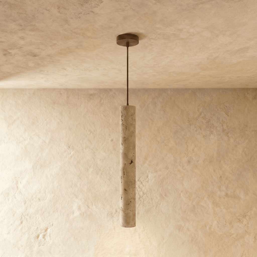Clérachic slim travertine-look cylinder pendant on a thin dark rod and bronze ceiling plate, against limewash walls.