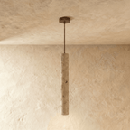 Clérachic slim travertine-look cylinder pendant on a thin dark rod and bronze ceiling plate, against limewash walls.