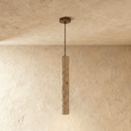 Clérachic slim travertine-look cylinder pendant hanging from a round bronze ceiling plate in a mid length on limewash.