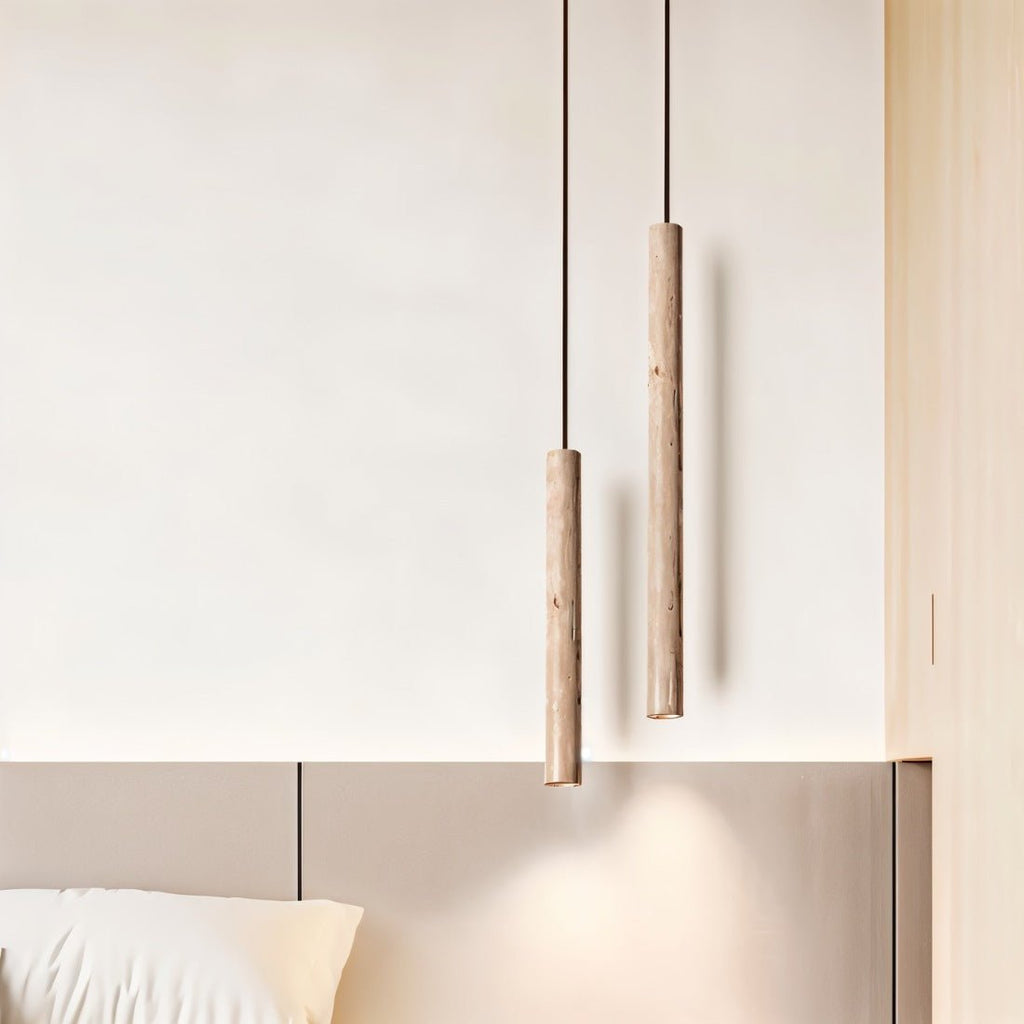 Clérachic two slim stone-look cylinder pendants at staggered heights above a bedhead, with a soft pool of light below.