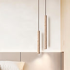 Clérachic two slim stone-look cylinder pendants at staggered heights above a bedhead, with a soft pool of light below.