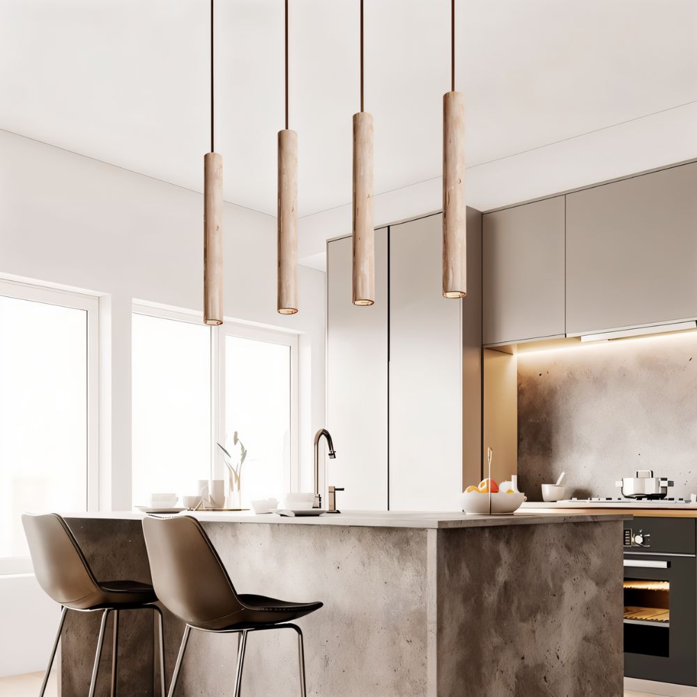 Clérachic row of four slim stone-look cylinder pendants hung at varied heights above a concrete-look kitchen island.