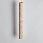 Clérachic close view of a slim travertine-look cylinder pendant showing its pitted, natural stone texture on a grey wall.