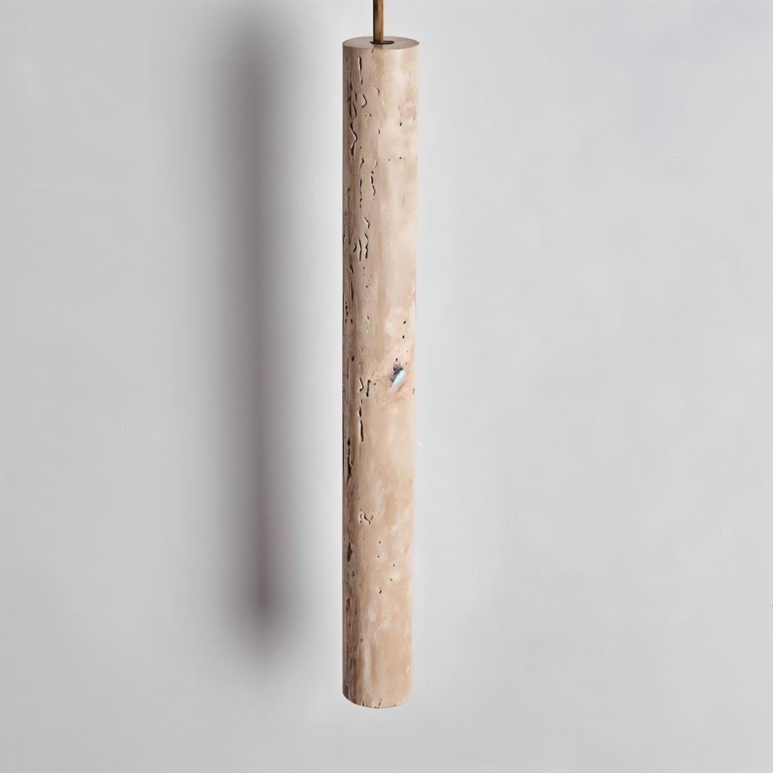 Clérachic close view of a slim travertine-look cylinder pendant showing its pitted, natural stone texture on a grey wall.