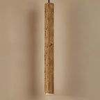 Clérachic lit slim travertine-look cylinder pendant close up, warm pitted stone grain and a glowing opening at the base.