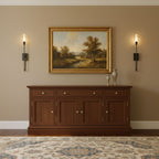 Two slim black Clérachic wall sconces either side of a framed landscape above a mahogany sideboard, on a warm taupe wall.