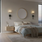 A pair of black Clérachic wall sconces above a bedroom's headboard wall, either side of a round brass-framed mirror, beside a pale floating nightstand.