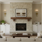 Brass Clérachic sconces on beige walls either side of a stone fireplace with a wood mantel and a framed landscape, with white cabinets beyond.