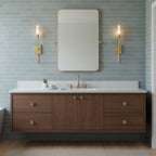 Two lit brass Clérachic wall lights either side of a tall rounded mirror on pale blue tiles, above a walnut floating vanity with a white top.