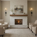 Black Clérachic sconces with frosted tubes either side of a white-brick fireplace and wood mantel, with cream armchairs on a patterned rug.