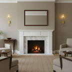 Slim brass Clérachic sconces at either side of a framed mirror above a white marble fireplace, in a calm taupe living room with a lit fire.