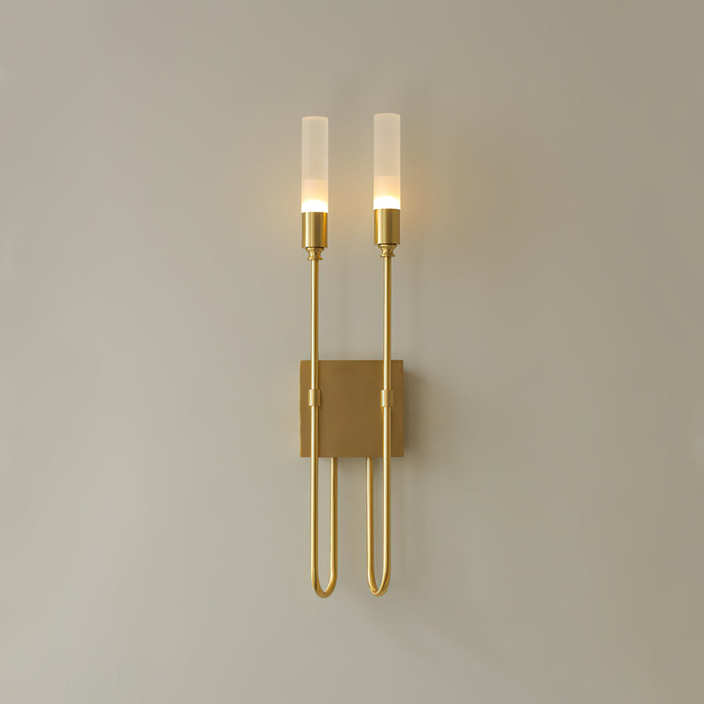 Antique brass finish on this Clérachic two-light sconce, its frosted tubes softly lit against a plain beige wall.