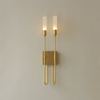 Antique brass finish on this Clérachic two-light sconce, its frosted tubes softly lit against a plain beige wall.