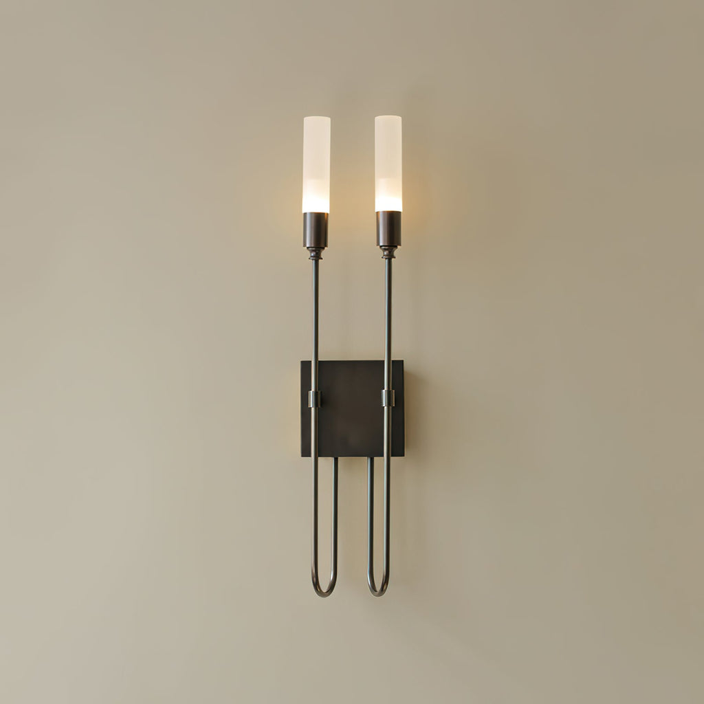 Dark black two-light Clérachic sconce on a plain beige wall, both frosted tubes lit above a square plate.