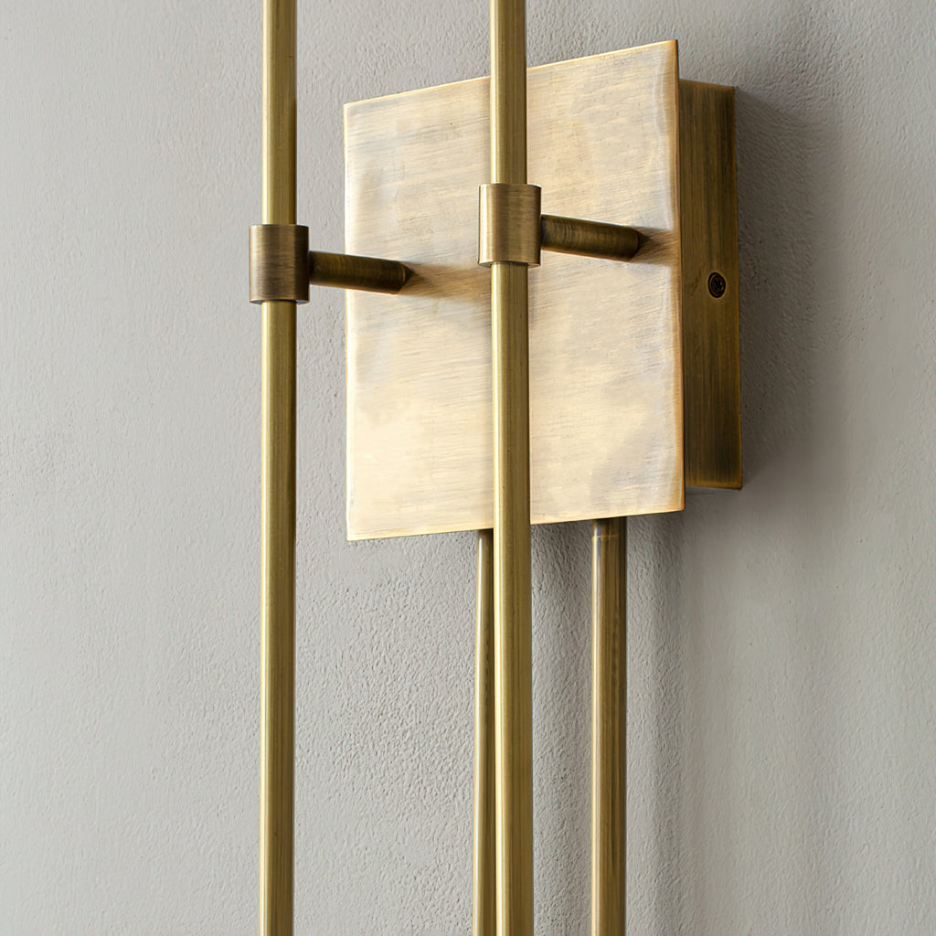 Close view of the aged brass backplate, clamps and upright arms of this Clérachic sconce on a grey textured wall.