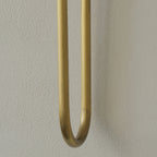 Close view of the rounded U-bend at the base of a brass arm on this Clérachic sconce, against a textured grey wall.