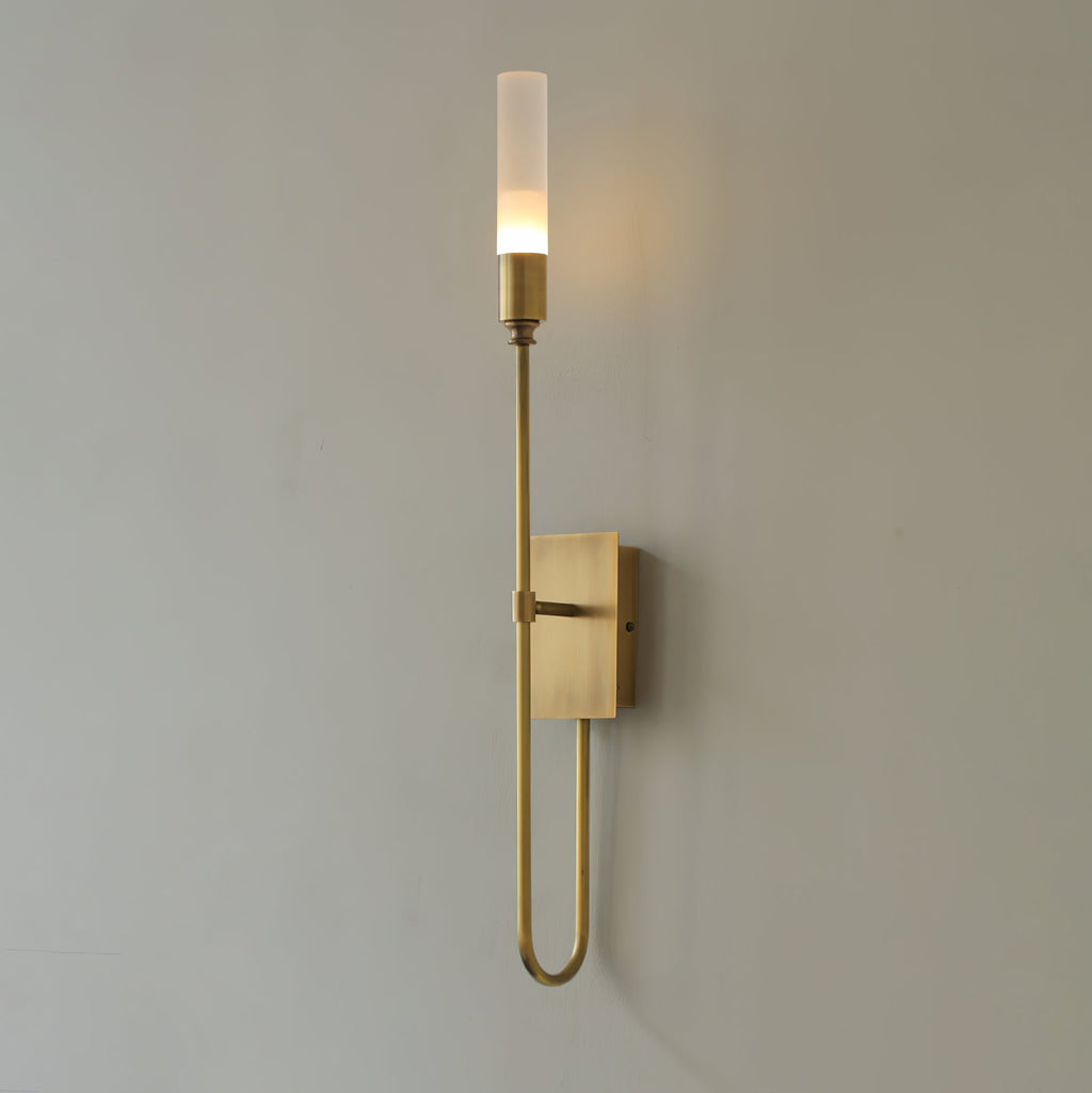 Single-light Clérachic sconce in antique brass on a grey wall, with a long looped arm curving below the small backplate.