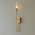 Single-light Clérachic sconce in antique brass on a grey wall, with a long looped arm curving below the small backplate.