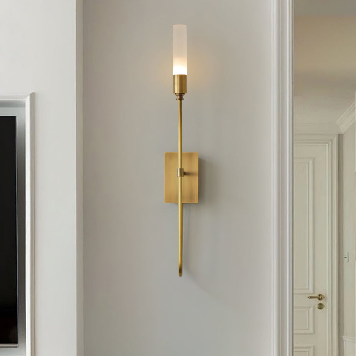 Single-light brass Clérachic sconce on a grey wall near a white doorway, its frosted tube softly lit.