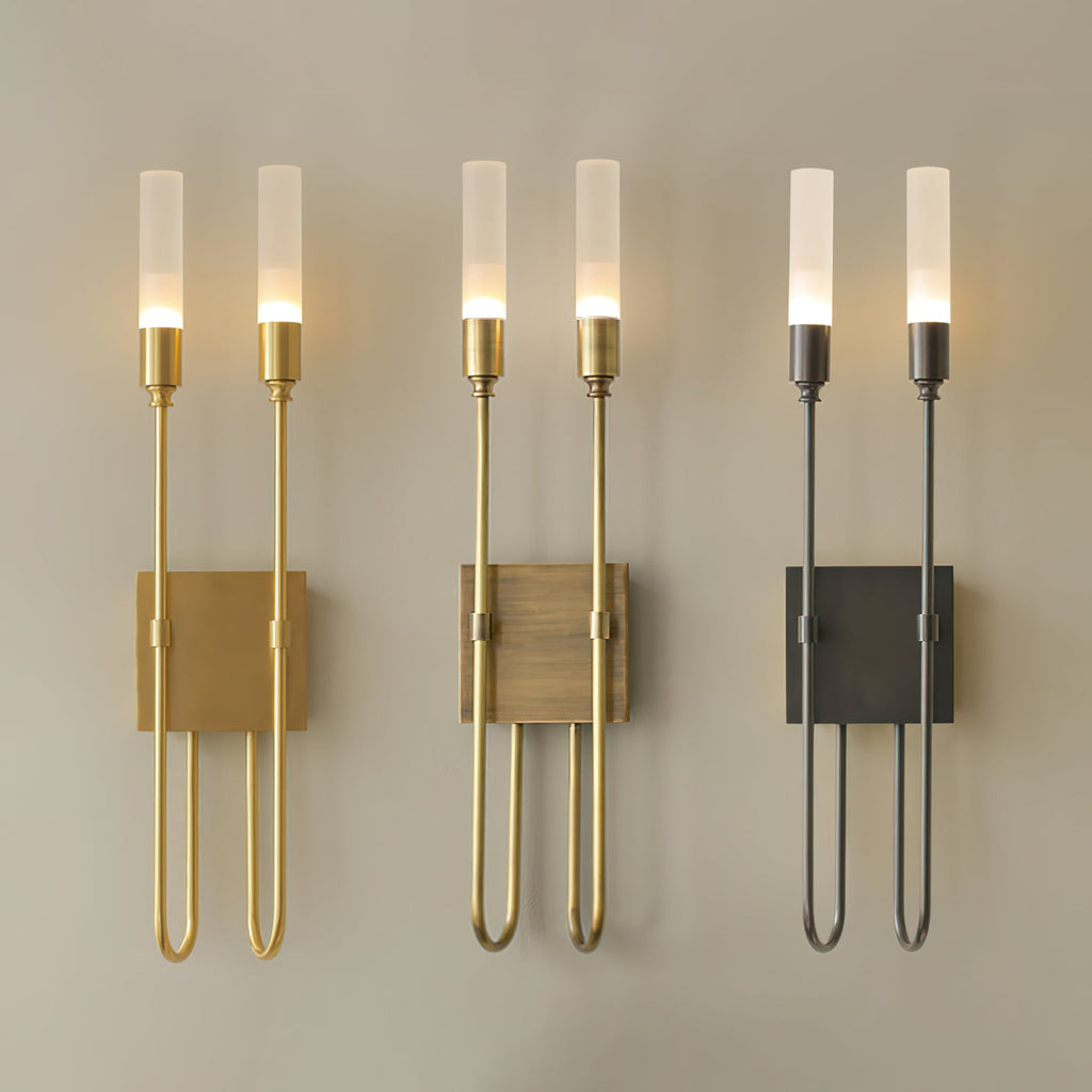 Three two-light Clérachic sconces in a row on a beige wall, in brass, antique brass and black, with the frosted tubes lit.