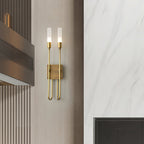 Distant view of a brass two-light Clérachic sconce on a pale panelled wall beside a marble-look panel and a dark metal vent.