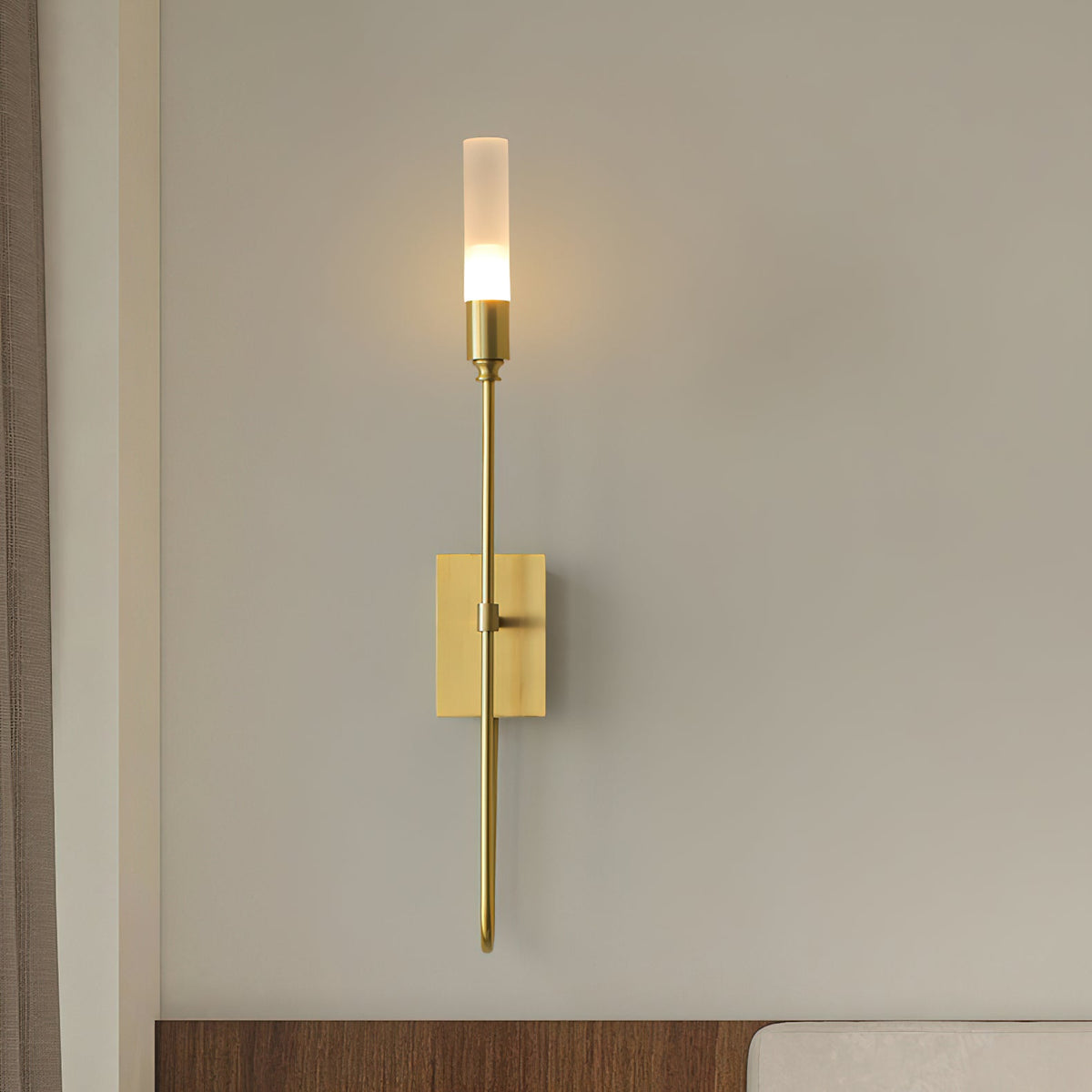 Brass single-light Clérachic sconce lit on a grey wall above a walnut shelf edge and a cream sofa.
