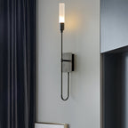 Black single-light Clérachic sconce with a looped lower arm, on a grey wall beside dark navy curtains.