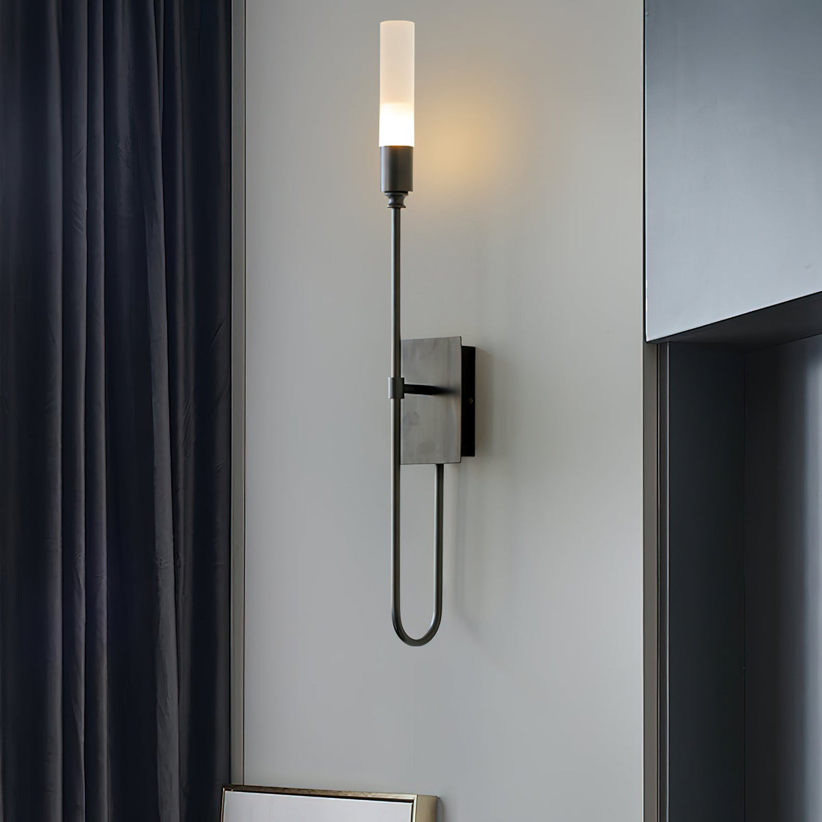 Black single-light Clérachic sconce with a looped lower arm, on a grey wall beside dark navy curtains.