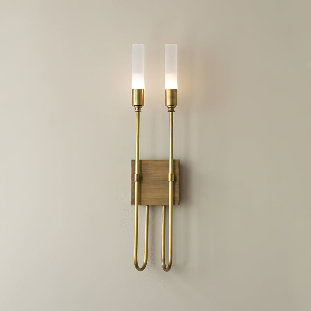 Two-light Clérachic sconce in antique brass on a warm neutral wall, both frosted tubes lit above a small square plate.