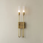 Two-light Clérachic sconce in antique brass on a warm neutral wall, both frosted tubes lit above a small square plate.