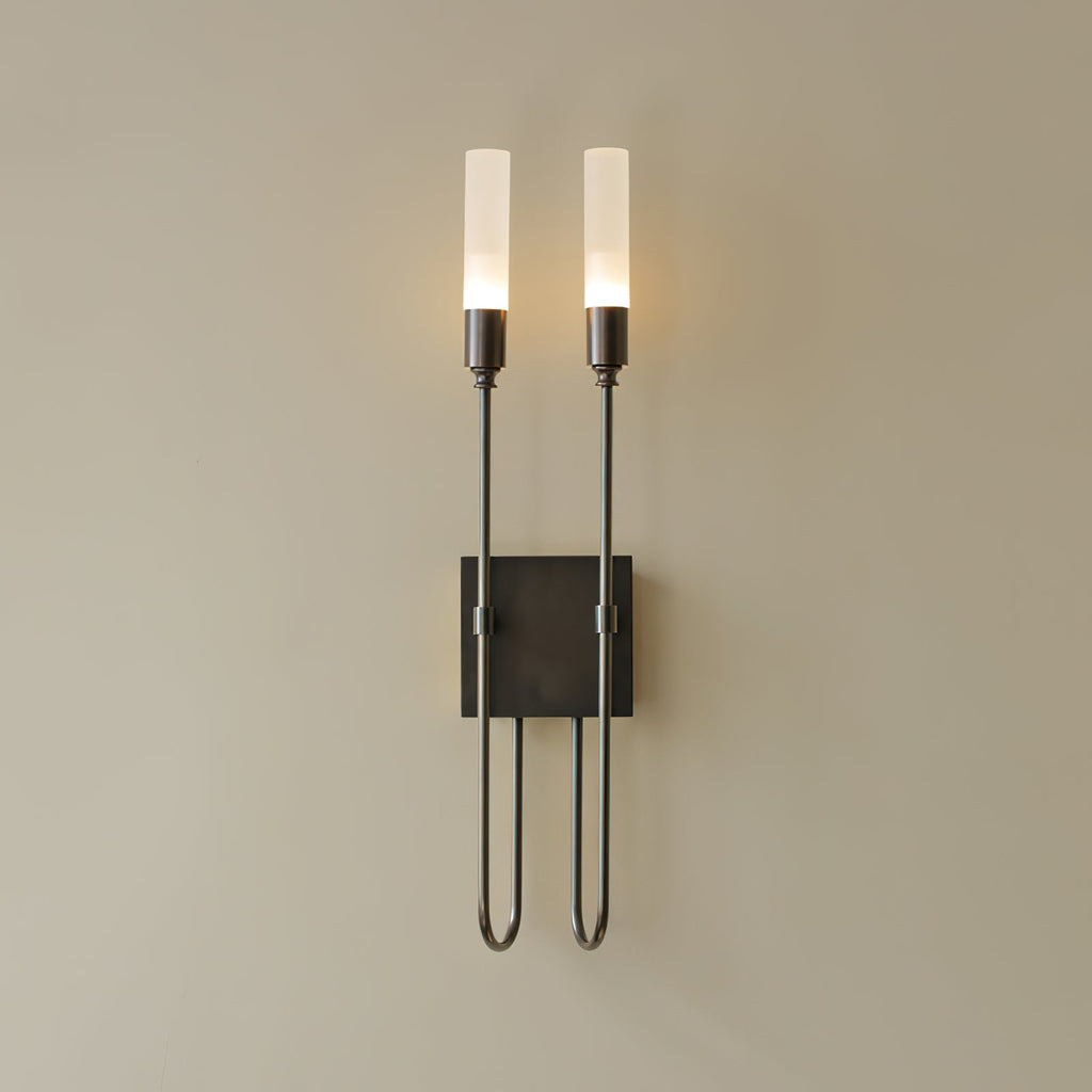 Black two-light Clérachic sconce on a beige wall, with both frosted tubes lit and thin arms dropping to a looped base.