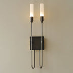 Tall view of this black Clérachic two-light sconce, lit, with its square plate and U-shaped arms on a beige wall.
