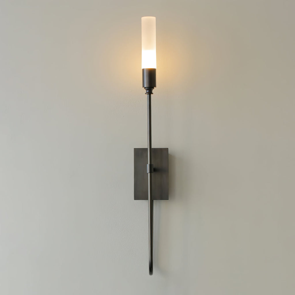 Single-light black Clérachic sconce on a grey wall, its frosted tube glowing above a small dark rectangular plate.