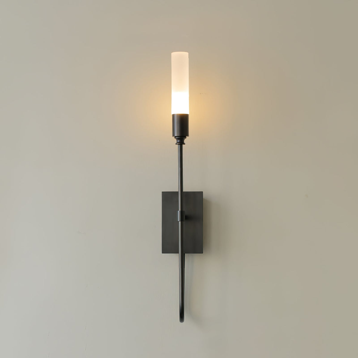 Black single-light Clérachic sconce lit on a taupe wall, with a slender arm below a small square plate.