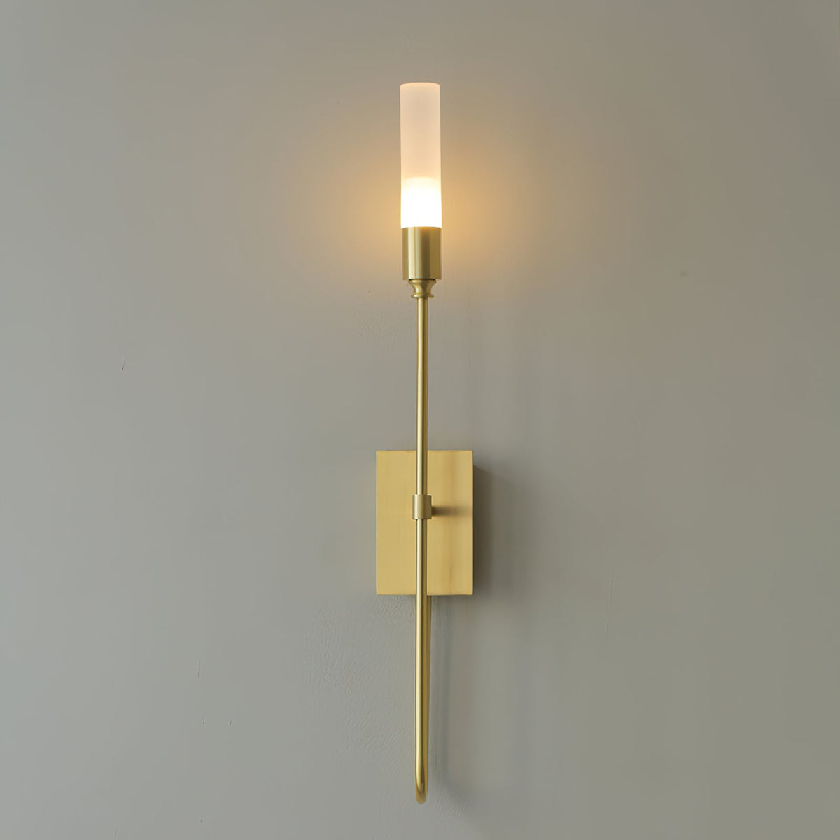 Single-light brass Clérachic sconce with a glowing frosted tube on a grey wall, a long straight arm below the plate.
