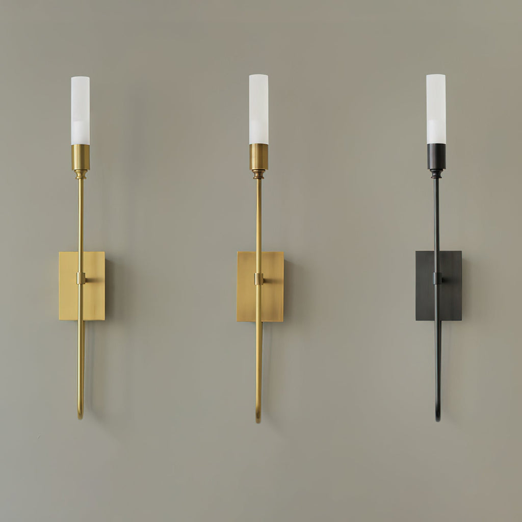Three single-light Clérachic sconces on a grey wall, in brass, antique brass and black, with the frosted tubes lit.