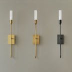 Three single-light Clérachic sconces on a grey wall, in brass, antique brass and black, with the frosted tubes lit.