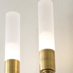 Close view of two frosted tubes with brass collars on this Clérachic sconce, glowing warm against a pale wall.