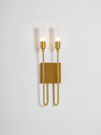 Brass two-light Clérachic sconce on a pale backdrop with both frosted tubes lit and the plate in warm light.